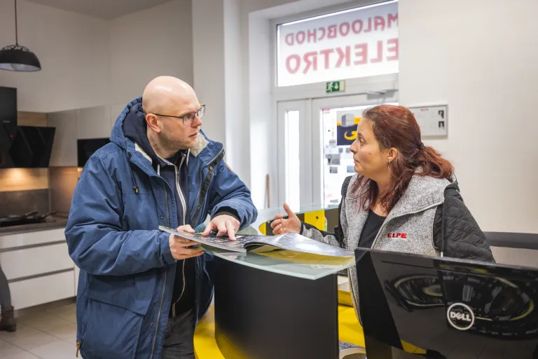 Dva zaměstnanci ELPE diskutují u recepce nad dokumenty v kanceláři