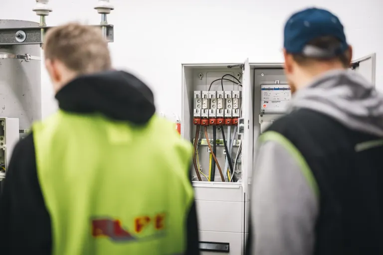 Dva elektrikáři kontrolují rozvaděč s jističemi a elektroměrem při práci