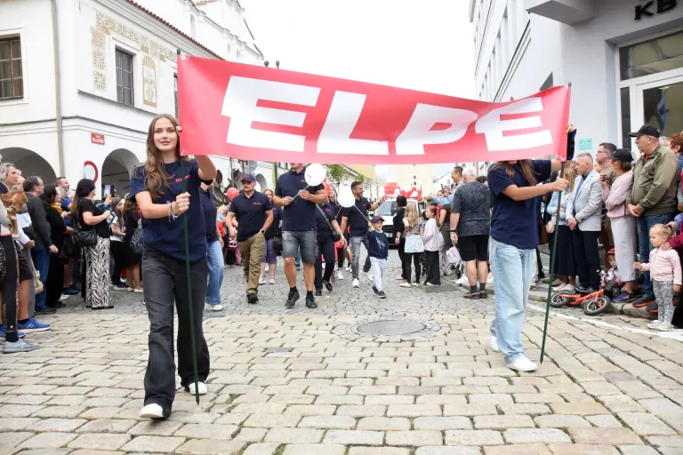 Členové týmu nesou červený transparent ELPE při průvodu na dlážděné ulici