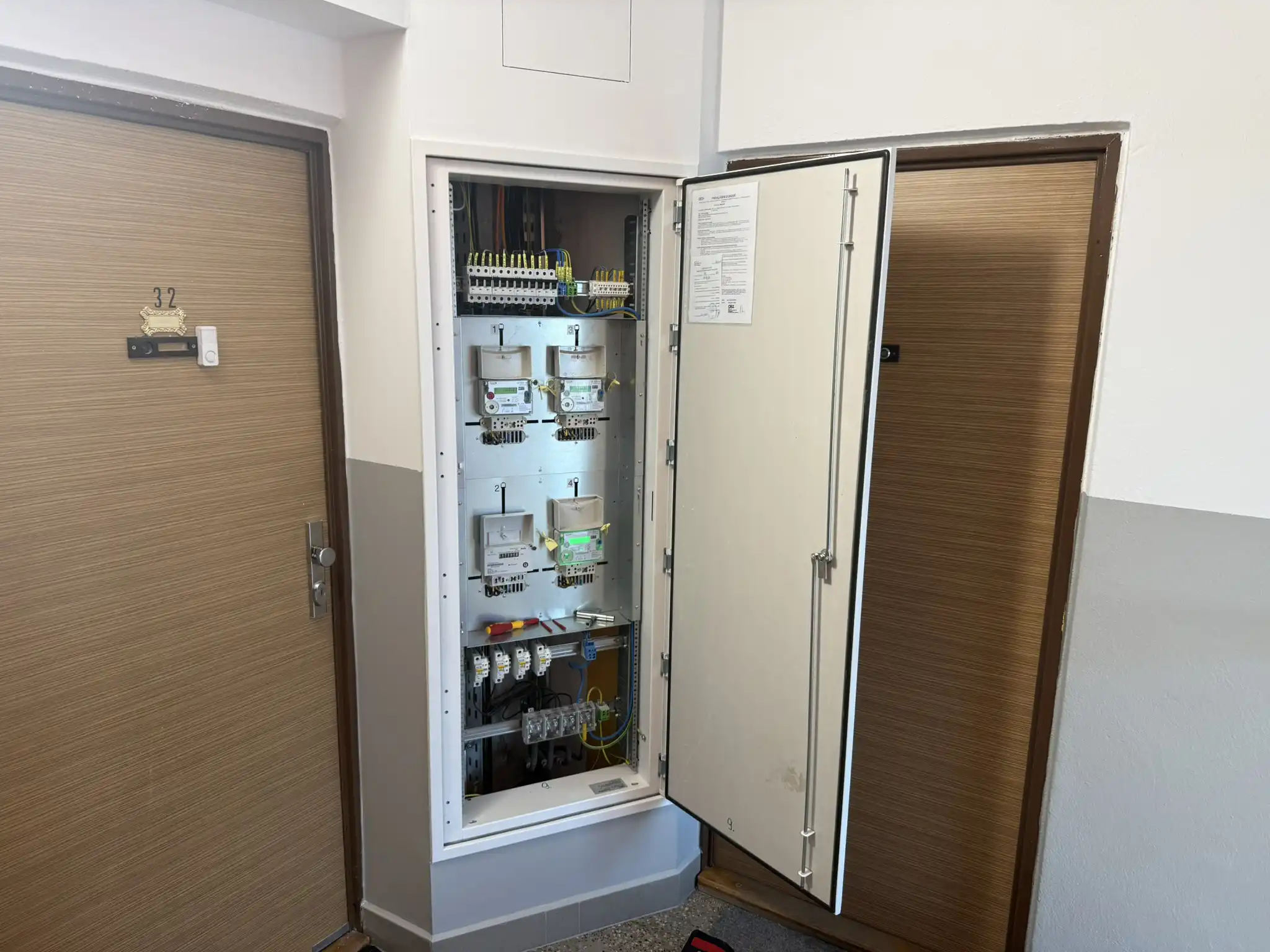 Elektroměrový rozvaděč s otevřenými dveřmi v chodbě bytového domu