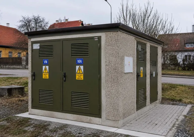 Venkovní trafostanice s kovovými dveřmi a výstražnými tabulkami v obci