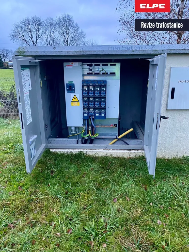 Otevřená venkovní trafostanice s elektrickými rozvody a jističem na travnatém pozemku