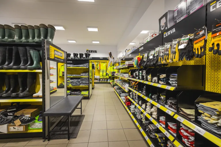 Interiér prodejny pracovních oděvů a obuvi s regály plnými rukavic, bot a reflexních vest