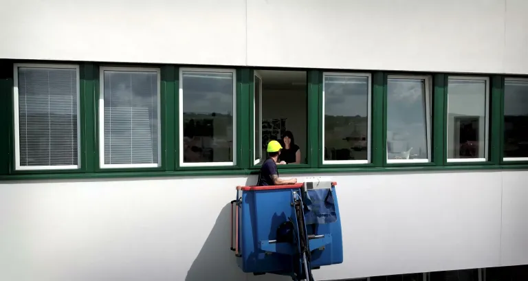 Pracovník ELPE v koši autoplošiny u okna ve výšce