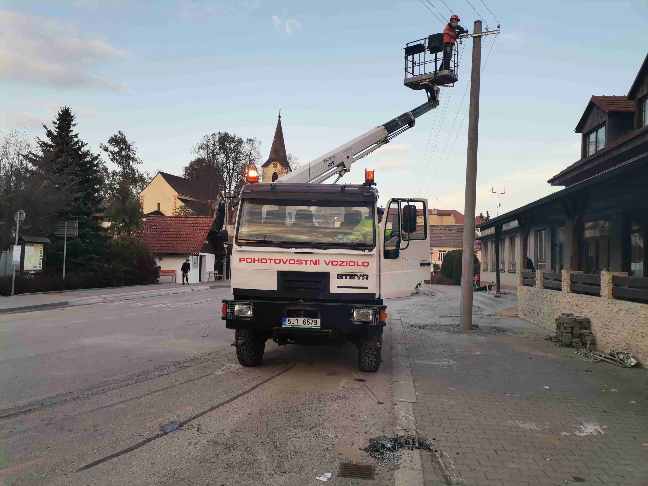 Pracovník na plošině opravuje vedení na sloupu veřejného osvětlení v obci