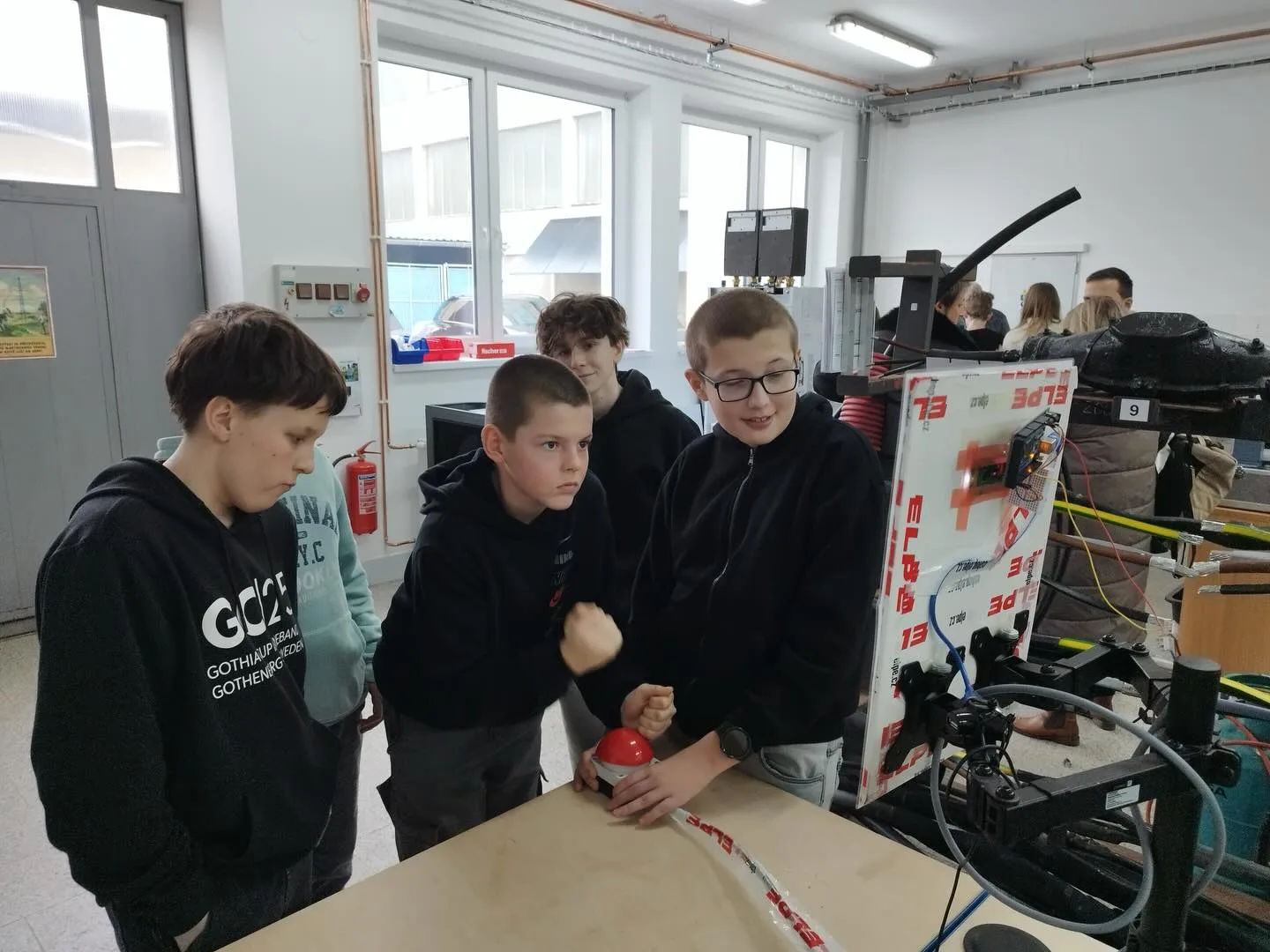 Skupina chlapců u montážního stolu v dílně s elektrozařízením