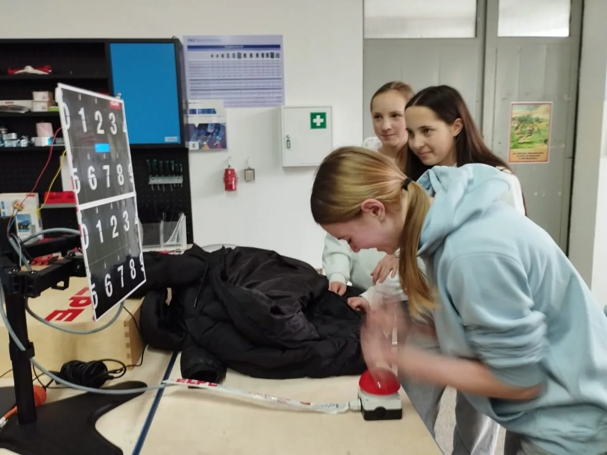 Tři žákyně sledují výukový panel s tlačítkem ve výukovém polygonu ELPE