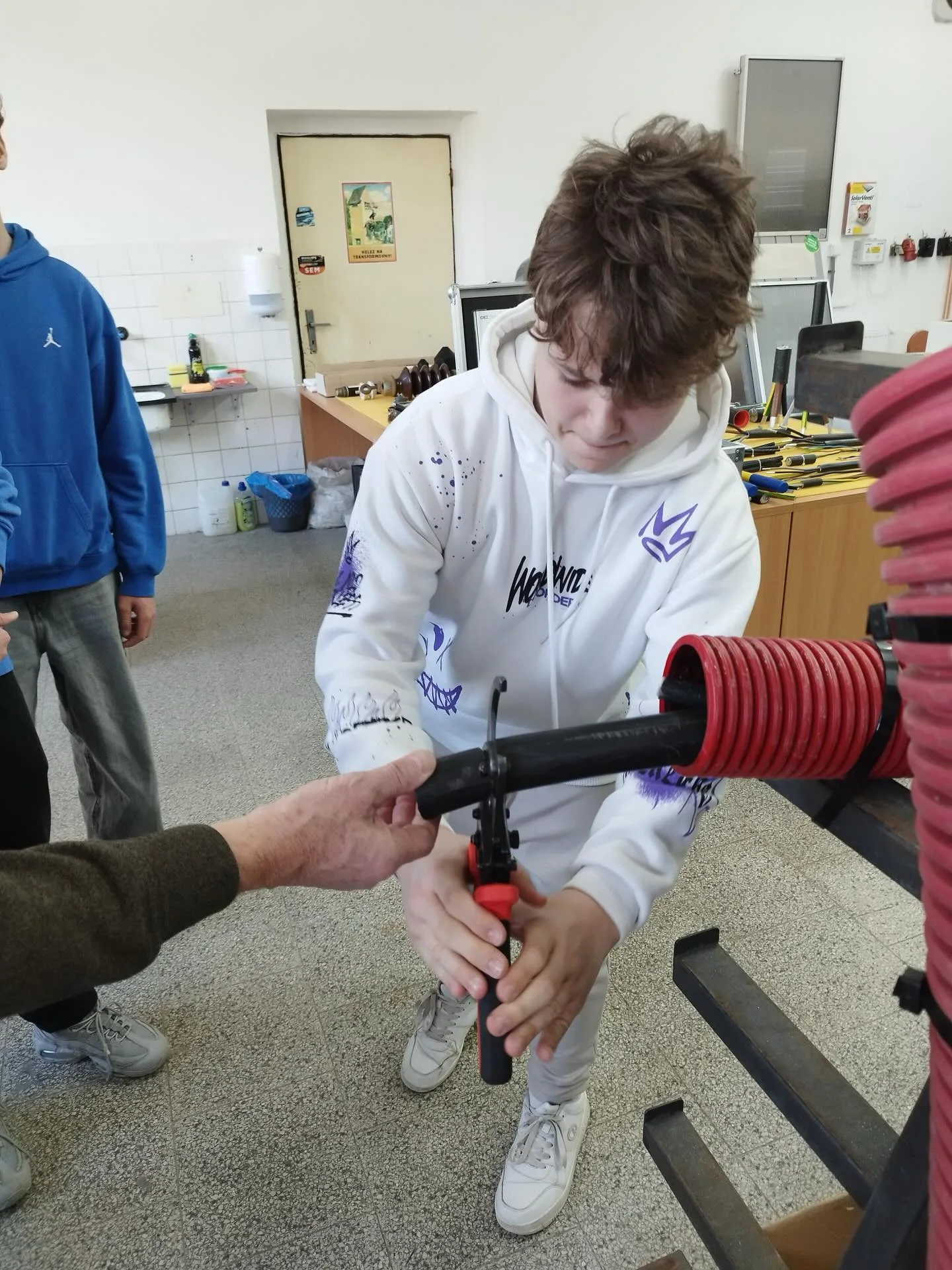 Technik předává žákovi nářadí v dílně při praktické ukázce