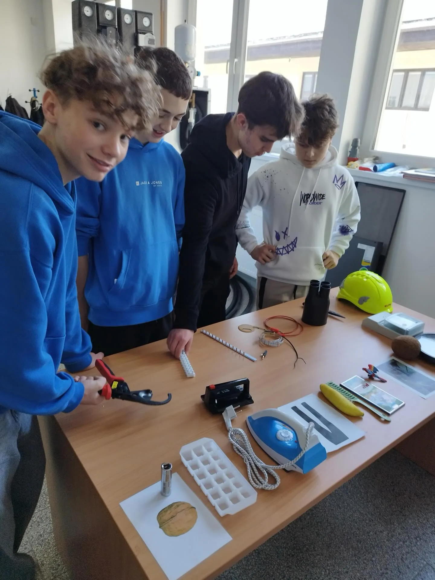 Čtyři mladí lidé u pracovního stolu s elektrickými komponenty a nářadím v dílně nebo učebně
