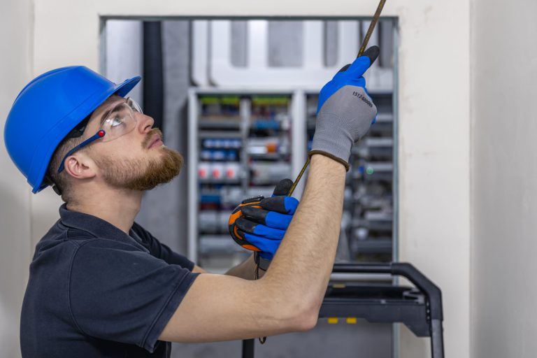 Elektromontér s přilbou a rukavicemi instaluje kabeláž ve stropě bytového domu